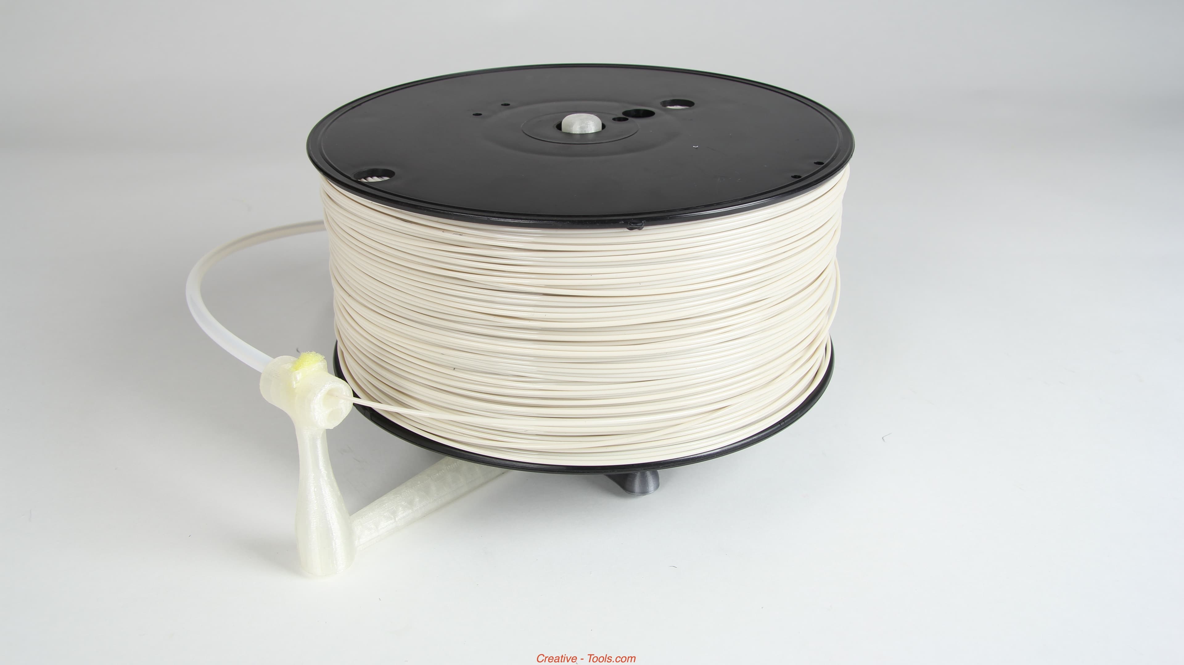 Fotografía de una bobina blanca de filamento FDM colocada sobre un soporte de sobremesa impreso en 3D