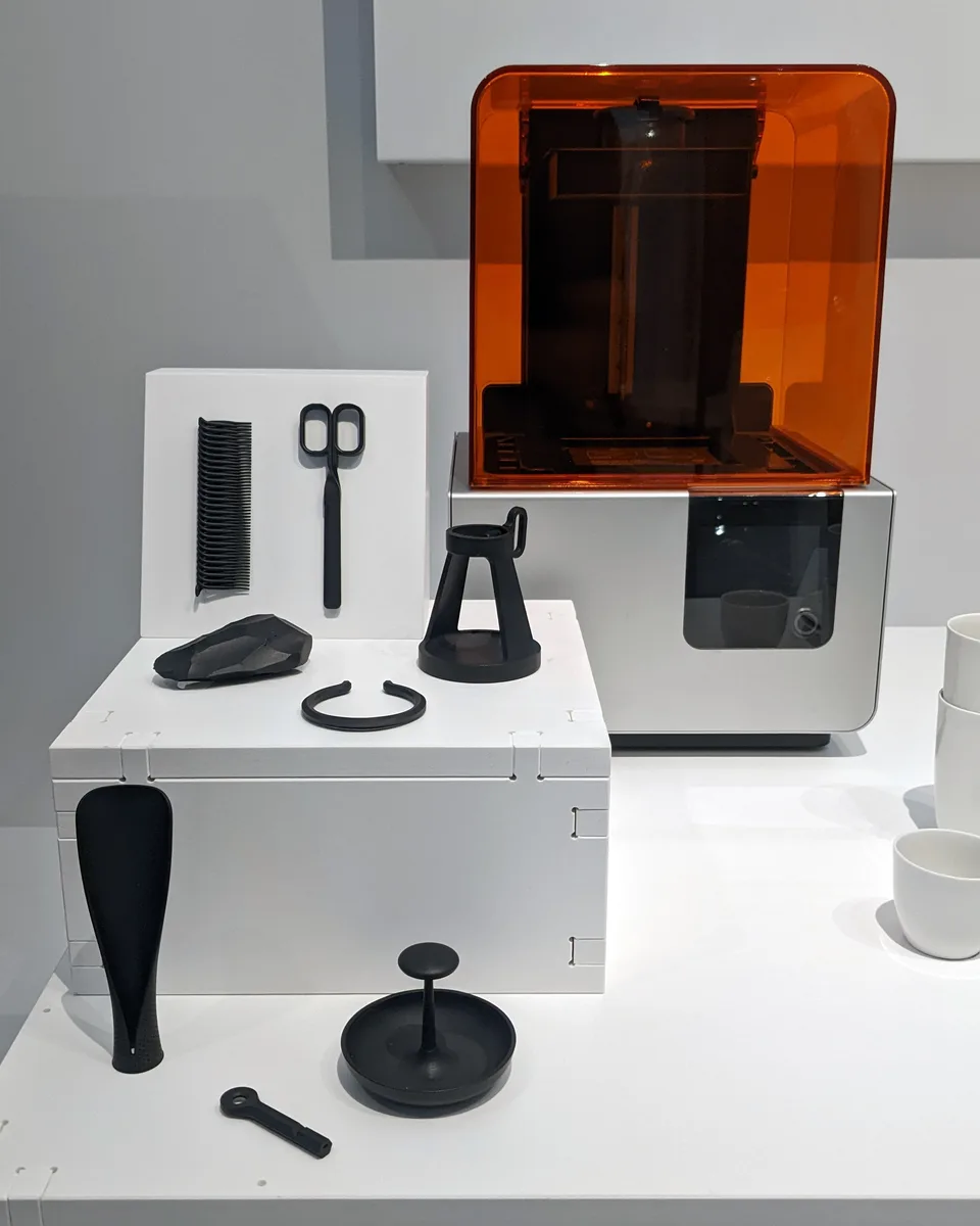 Impresora de resina Formlabs Form 2 con cubierta naranja y piezas impresas en una exposicion.